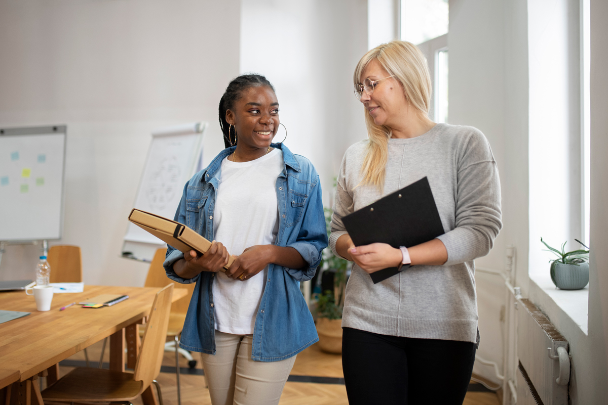 professional female walks and talks to younger female in office 